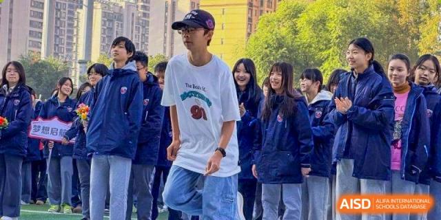 A student in a white graphic t-shirt and baseball cap stands with classmates at Wuxi Foreign Language School International Curriculum Center.