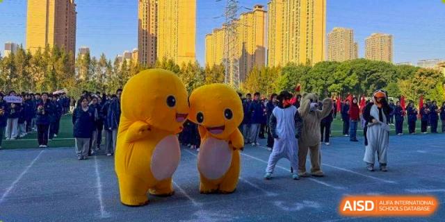 Two large yellow bird mascots stand on an athletic field during a sports day at Wuxi Foreign Language School International Curriculum Center.