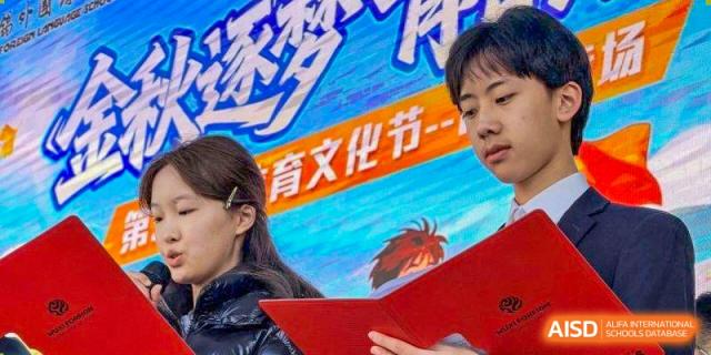 A student holds a red folder while standing in front of a colorful event banner at Wuxi Foreign Language School International Curriculum Center.