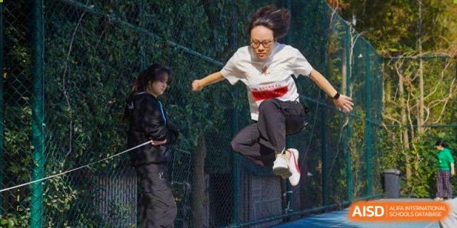 An athlete mid-air during a competitive long jump event on an outdoor track at Wuxi Foreign Language School International Curriculum Center.
