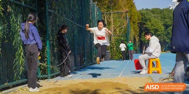 A student in a white t-shirt performs a long jump into a sandpit during a track meet at Wuxi Foreign Language School International Curriculum Center.