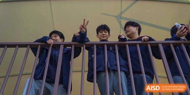 A group of students leans over a railing and gives a peace sign at Wuxi Foreign Language School International Curriculum Center.