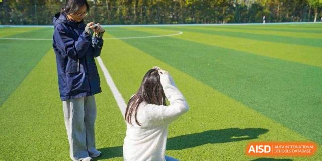 A student in a white sweater sits on a green turf field during an event at Wuxi Foreign Language School International Curriculum Center.