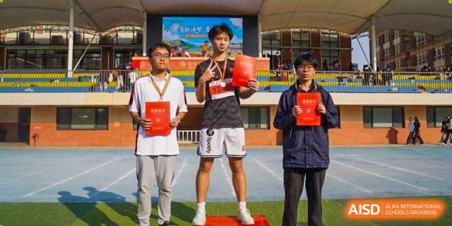 Three students posing with red award certificates on a winner's podium at Wuxi Foreign Language School International Curriculum Center.