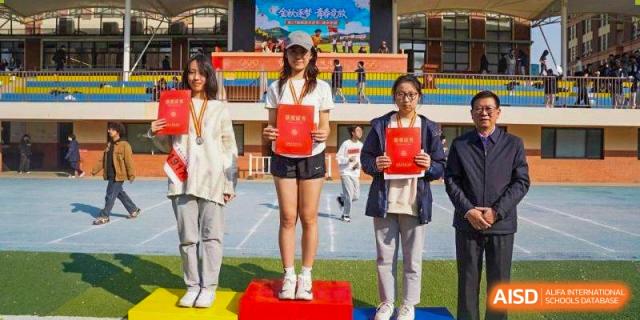 A female student athlete stands on the first-place podium holding her award certificate at Wuxi Foreign Language School International Curriculum Center.