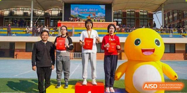 Three students stand on a podium displaying their red award folders and medals at Wuxi Foreign Language School International Curriculum Center.