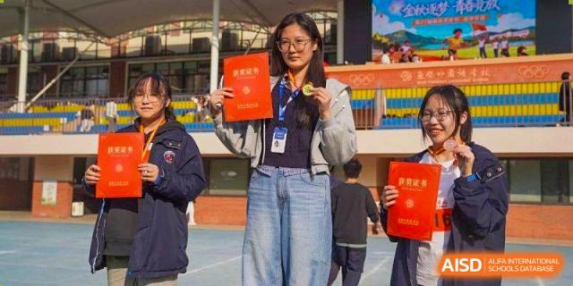 A female student wearing a grey jacket holds up her red merit certificate and gold medal at Wuxi Foreign Language School International Curriculum Center.