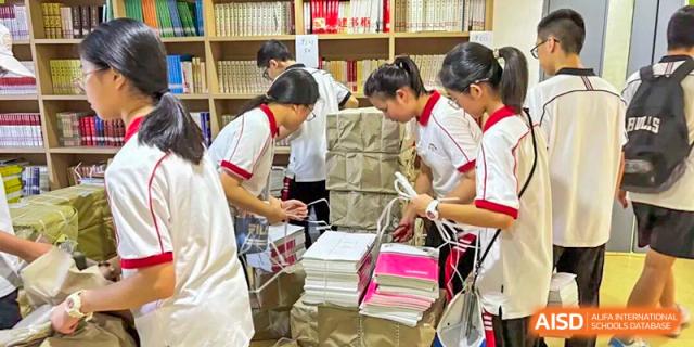 Students in white and red uniforms work together to organize and stack large bundles of books and educational materials at Wenzhou Foreign Language School.