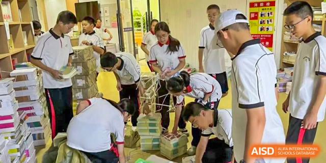 A group of students in a bright hallway collaborate on a hands-on project involving structural materials and stacked papers at Wenzhou Foreign Language School.