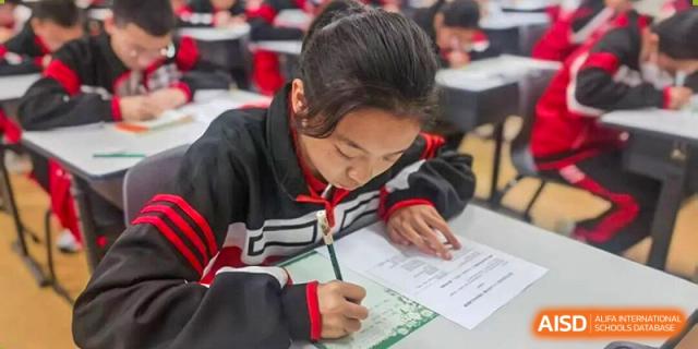 A close-up of a student focused on writing an exam or worksheet at a wooden desk at Wenzhou Foreign Language School.
