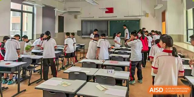 Students in white uniforms gather and organize materials in a classroom setting at Wenzhou Foreign Language School.