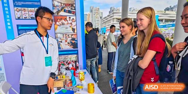 Students and visitors browse a vibrant technology exhibition booth featuring 3D-printed models and creative projects at Wenzhou Foreign Language School.