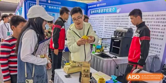 An instructor demonstrates a complex yellow mechanical model to attentive students during a hands-on engineering workshop at Wenzhou Foreign Language School.