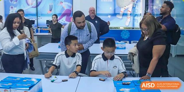 Two students sit at a desk working on electronic circuit boards and wiring under the guidance of instructors at Wenzhou Foreign Language School.