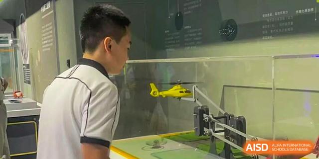 A student observes a yellow scale-model helicopter mounted inside a specialized aerodynamic testing chamber at Wenzhou Foreign Language School.