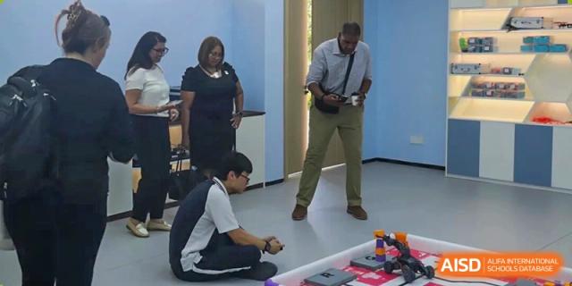 A student works on a robotics project on the floor while instructors observe and provide guidance during a practical session at Wenzhou Foreign Language School.