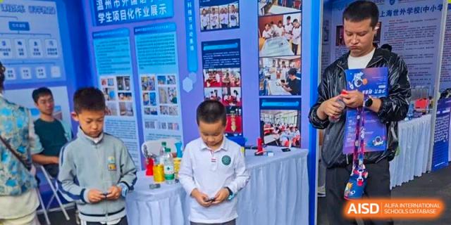 A young student in a white polo shirt examines a small object in front of an educational display board and project table at Wenzhou Foreign Language School.