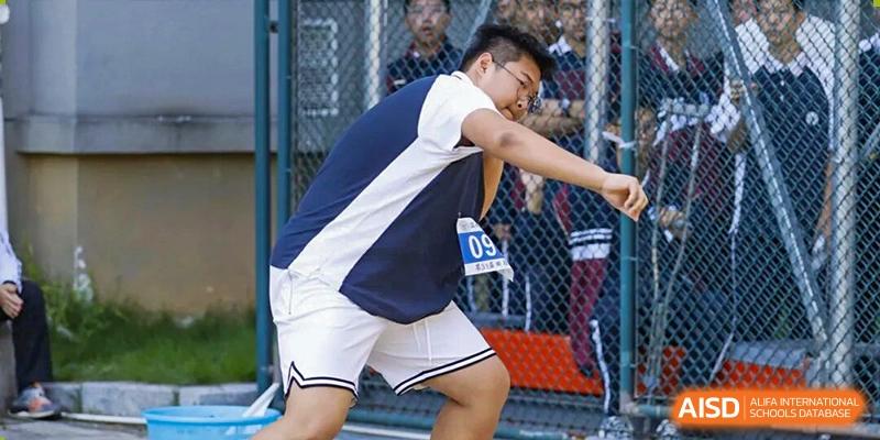 A young male student wearing a sports uniform and bib number 09 prepares for a shot put throw during a field event at Wenzhou Foreign Language School.