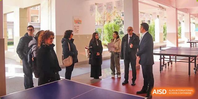 Four adults stand near an indoor table tennis table, engaged in a conversation or tour within a hallway at Wenzhou Foreign Language School.