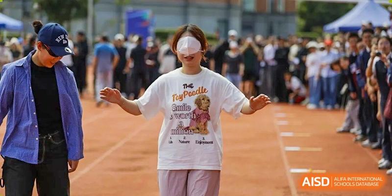 A smiling student wearing a graphic T-shirt and a blindfold participates in an outdoor sensory or team-building activity at Wenzhou Foreign Language School.