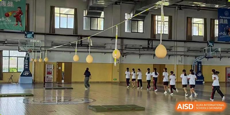 Students participate in a physical education class in a large indoor gymnasium featuring hanging targets and floor mats at Wenzhou Foreign Language School.