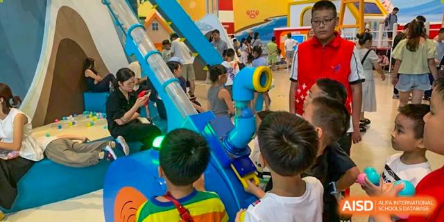 Children interacting with a colorful, blue science exhibit or playground equipment during an indoor activity at Wenzhou Foreign Language School.
