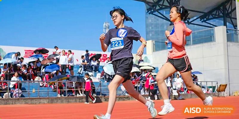 A female student runner wearing bib number 2223 competing in a track race on an outdoor red track at Wenzhou Foreign Language School.