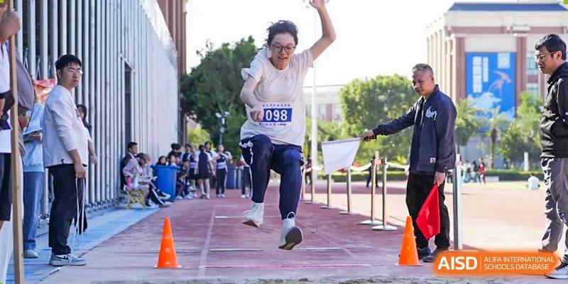 A female student mid-air while performing a long jump into a sand pit during a sports event at Wenzhou Foreign Language School.