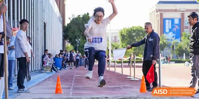 A female student mid-air while performing a long jump into a sand pit during a sports event at Wenzhou Foreign Language School.