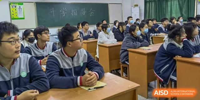 A student sits attentively at a wooden desk while focused on a presentation during a classroom lecture at XuZhou No.3 Middle School.