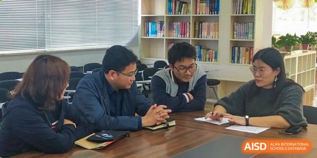 Two male students engage in a collaborative discussion while seated at a table during a workshop at XuZhou No.3 Middle School.
