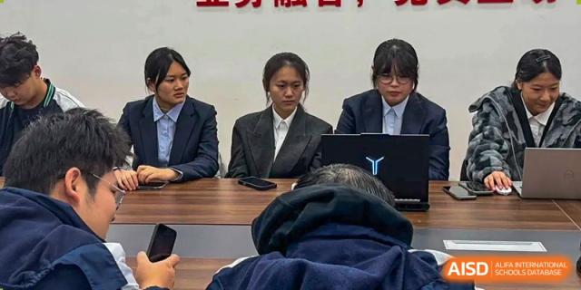 Three students in formal business attire sit at a conference table during a school presentation at XuZhou No.3 Middle School.