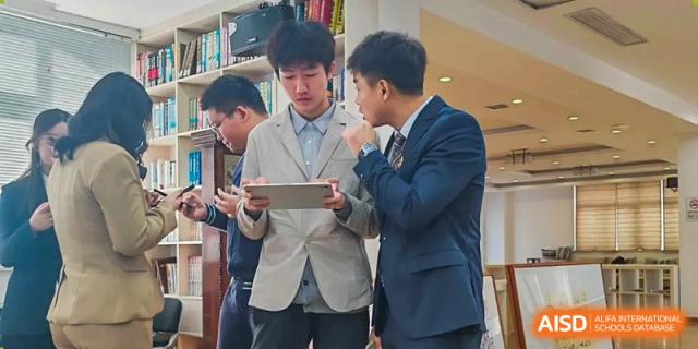 Two male students in suits collaborate while looking at a tablet during a formal school event at XuZhou No.3 Middle School.