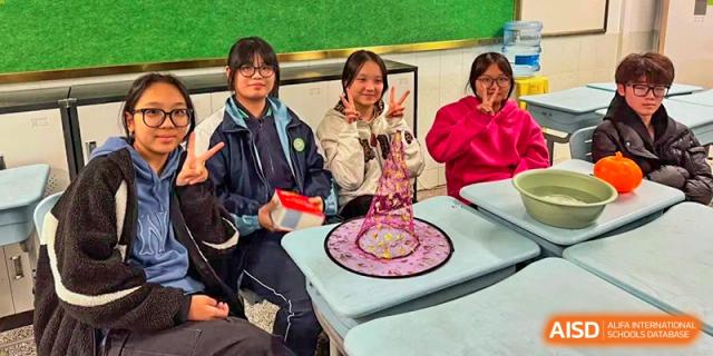 Three female students smile and pose while showing off a creative pink mesh craft project at their desks at XuZhou No.3 Middle School.