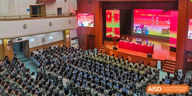 A wide overhead view shows a large assembly of students in uniform seated in a spacious auditorium during a formal presentation at XuZhou No.3 Middle School.