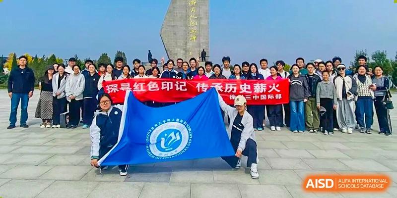 Students stand outdoors holding a large red banner and a blue school flag during a commemorative field trip at XuZhou No.3 Middle School.
