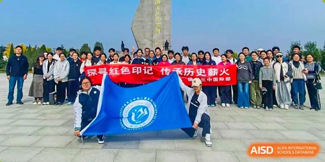 Students stand outdoors holding a large red banner and a blue school flag during a commemorative field trip at XuZhou No.3 Middle School.