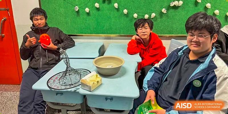 A student in a bright red hoodie rests at a light blue desk in a classroom decorated with green wall displays at XuZhou No.3 Middle School.