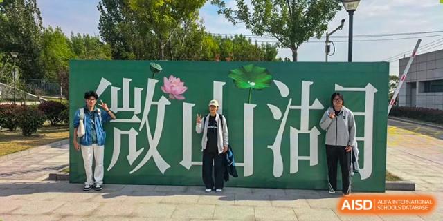A student poses for a photo in front of a large green mural featuring traditional Chinese characters and lotus flowers at XuZhou No.3 Middle School.