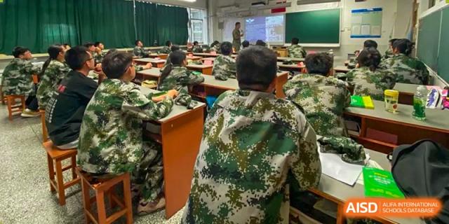 Students in camouflage uniforms sit at their wooden desks while listening to a lecture at the front of the classroom at XuZhou No.3 Middle School.