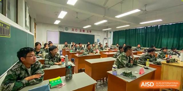 Students in camouflage uniforms sit at wooden desks in a modern classroom during an academic lesson at XuZhou No.3 Middle School.