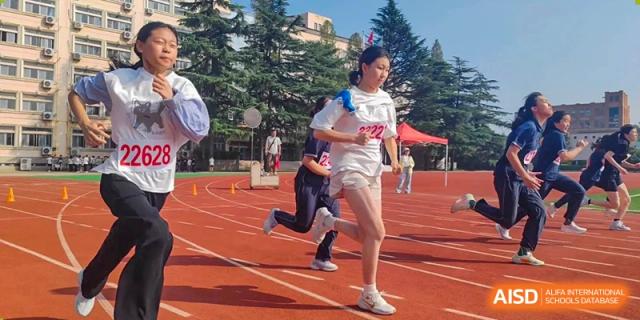 A student athlete in a white racing uniform competes in a track event on the red outdoor running grounds at XuZhou No.3 Middle School.