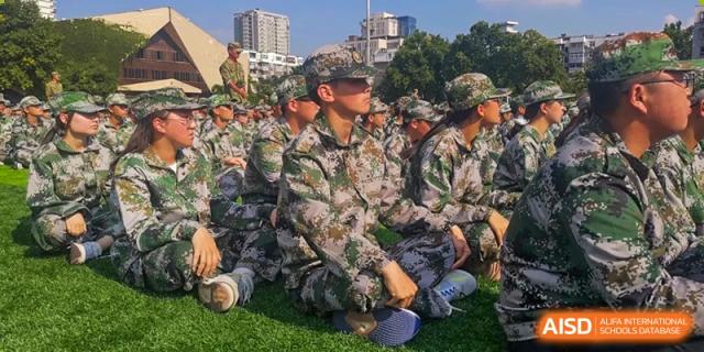 Students in full camouflage uniforms sit together on the grass field during a break from military training drills at XuZhou No.3 Middle School.