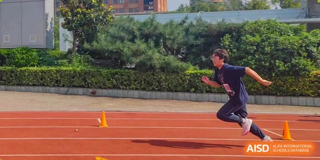 A focused athlete in a purple shirt prepares to start a sprint on the outdoor track during a sports competition at XuZhou No.3 Middle School.