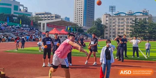 A student athlete in a pink jersey prepares to throw a shot put during an outdoor track and field meet at XuZhou No.3 Middle School.