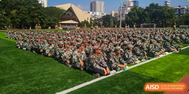 A massive assembly of students in camouflage gear sits in neat rows on the green sports field for a school event at XuZhou No.3 Middle School.