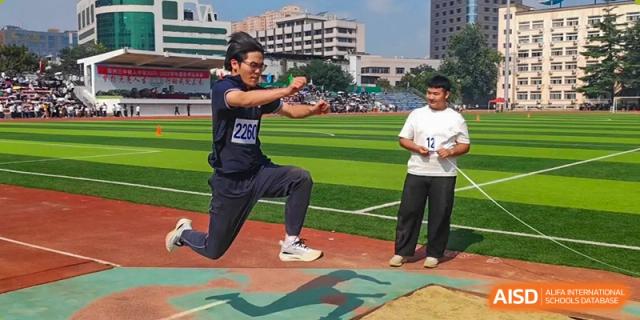A student athlete performs a long jump, captured mid-air above the sand pit during a physical education event at XuZhou No.3 Middle School.