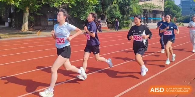 Female student athletes wearing numbered bibs compete in a long-distance race on the outdoor running track at XuZhou No.3 Middle School.