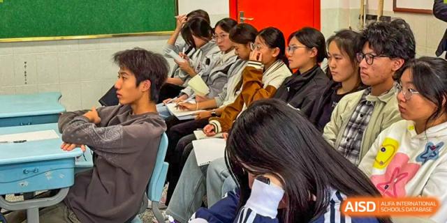 A row of students sits at their desks focused on taking notes during a lecture in a bright, modern classroom at XuZhou No.3 Middle School.