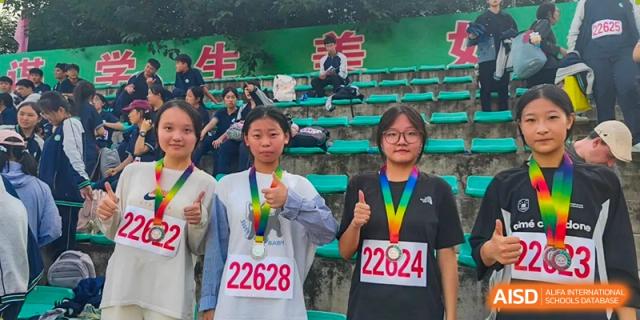 Two smiling female students proudly display their medals while wearing racing bibs after a track competition at XuZhou No.3 Middle School.